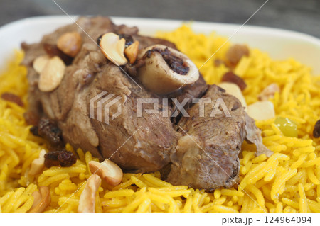 Enjoy a Savory Lamb Shank Served on Aromatic Yellow Rice Topped with Nuts 124964094