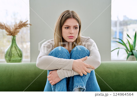 Unhappy upset young woman sitting on sofa at home, face close-up Unhappy upset young woman sitting on sofa at home, face close-up 124964564