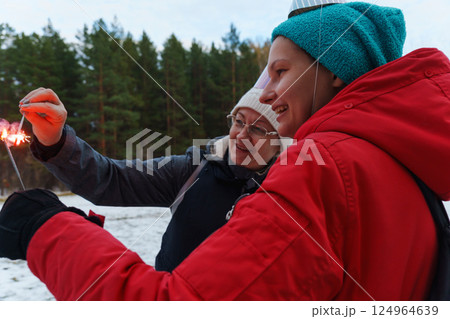 Celebration in the snowy forest with joyful individuals creating colorful sparks in winter Celebration in the snowy forest with joyful individuals creating colorful sparks in winter 124964639