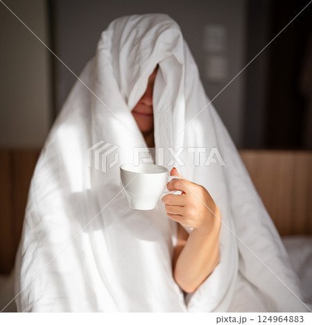 Woman with cup of coffee in the morning under the blanket at home Woman with cup of coffee in the morning under the blanket at home 124964883
