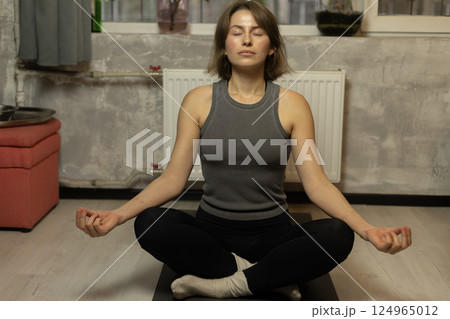 A woman meditates on a yoga mat at home A woman meditates on a yoga mat at home 124965012
