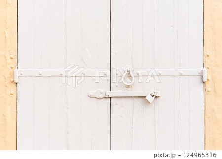 Closed vintage garage gates made of wooden palnks and an iron lock on it painted in beige and ochre colors 124965316