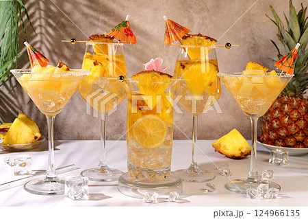 Various alcoholic cocktails with slices of mango, pineapple and ice in glasses with rims and umbrellas. Concept of a tropical party and relaxation. Advertising business card for a bar menu. 124966135