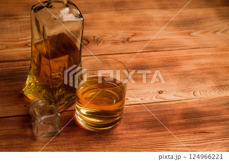 A glass and a decanter with whiskey stand on a wooden table. A glass and a decanter with whiskey stand on a wooden table. 124966221