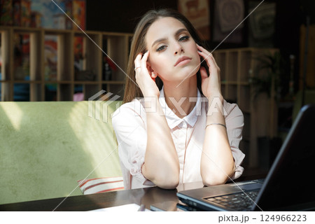 Beautiful girl at a table in a cafe is sitting in front of a laptop. 124966223