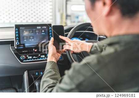 自動車の車内でスマホを使う自動車整備士の男性 自動車の車内でスマホを使う自動車整備士の男性 124969181