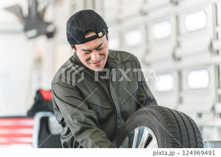 自動車整備工場でタイヤを運ぶ男性メカニック(肉体労働・重労働・重い・腰痛) 自動車整備工場でタイヤを運ぶ男性メカニック(肉体労働・重労働・重い・腰痛) 124969491