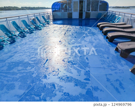 The morning sunlight reflected in droplets on the wet blue deck of the cruise ship, rows of sunbeds standing in a row 124969796