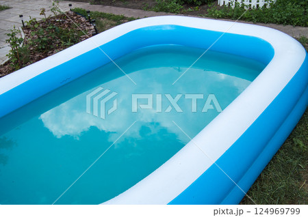 Close-up of an inflatable pool standing on the grass on a sunny summer day, the reflection of clouds on the surface of the water Close-up of an inflatable pool standing on the grass on a sunny summer day, the reflection of clouds on the surface of the water 124969799