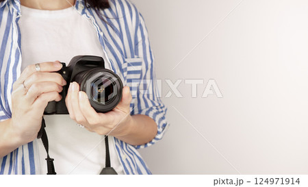 Photographer holding dslr camera. Self portrait, front view. Faceless nice woman with brown red hair in a tshirt with hands holding photo camera white background. Photographer holding dslr camera. Self portrait, front view. Faceless nice woman with brown red hair in a tshirt with hands holding photo camera white background. 124971914