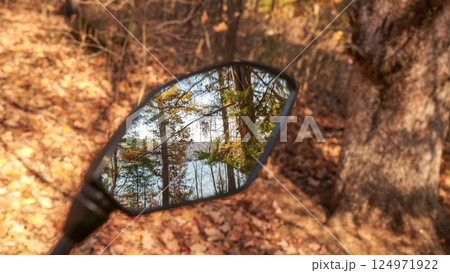 Rearview mirror view of a motorcycle showing a stunning lake and forest landscape in the distance 124971922