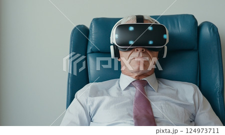 Elderly Man Engaged in Virtual Reality Experience While Seated Comfortably in Modern Chair 124973711