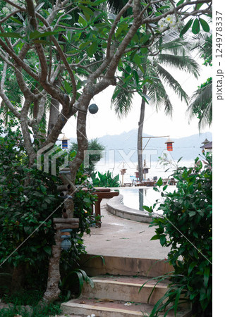 Lush greenery flanks a pathway leading directly to serene waters and palm trees.Thailand, Koh Phangan. 124978337