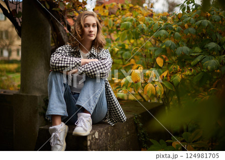 Beautiful Young Woman Sitting on a White Wooden Bench in a Tranquil Garden with Lush Greenery and Casual Attire Beautiful Young Woman Sitting on a White Wooden Bench in a Tranquil Garden with Lush Greenery and Casual Attire 124981705
