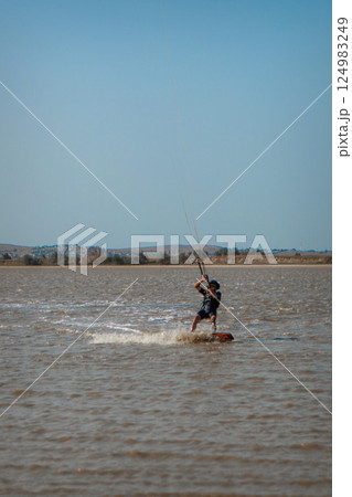A man, an athlete, rides kitersurfing on a blue pore. Beach, active recreation. Sunset competitions, parachute, board. High quality photo 124983249