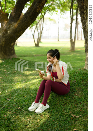 Smiling woman taking a break after workout using her smartphone with wireless earbuds Smiling woman taking a break after workout using her smartphone with wireless earbuds 124983513