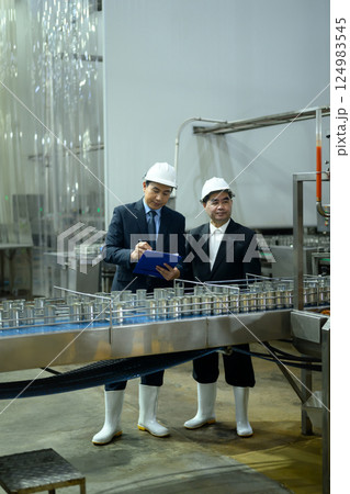 Factory supervisors in safety helmets examining a conveyor belt with metal cans in production plant 124983545