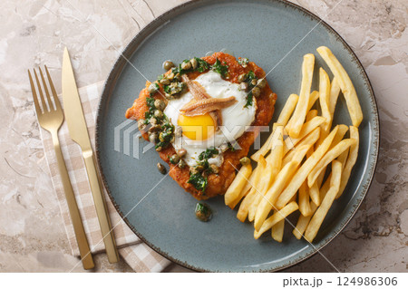 Delicious breaded schnitzel with anchovies, fried egg and capers parsley sauce on top served with french fries close-up on a plate. Horizontal top view 124986306