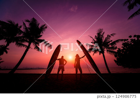 Silhouette of surfers couple holding long surf boards at sunset on tropical beach Silhouette of surfers couple holding long surf boards at sunset on tropical beach 124986775