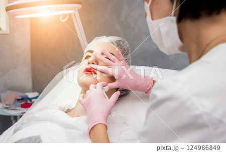 The doctor cosmetologist makes the facial injections procedure.  124986849