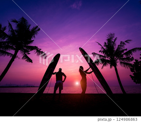 Silhouette of surfers couple holding long surf boards at sunset Silhouette of surfers couple holding long surf boards at sunset 124986863