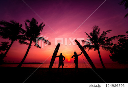 Silhouette of surfers couple holding long surf boards at sunset 124986893