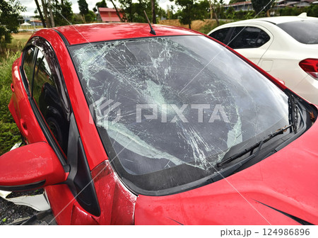 Shattered and broken windshield on a bright red car showcasing the damage to its glass surface Shattered and broken windshield on a bright red car showcasing the damage to its glass surface 124986896