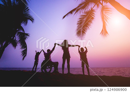 Disabled man in a wheelchair with his family on the beach. Silhouettes at sunset 124986900