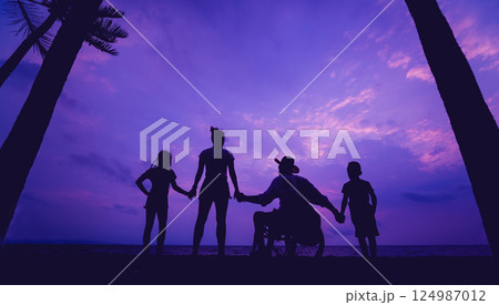 Disabled man in a wheelchair with his family on the beach. Silhouettes at sunset 124987012