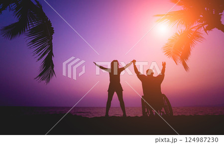 Disabled man in a wheelchair with his wife on the beach. Silhouettes at sunset 124987230