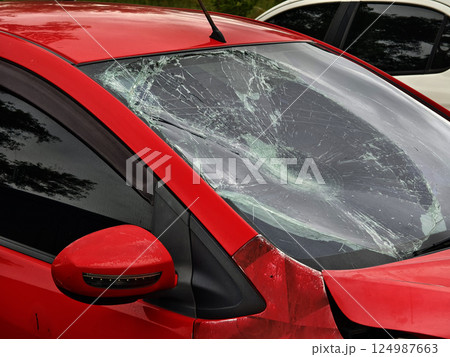 Shattered and broken windshield on a bright red car showcasing the damage to its glass surface Shattered and broken windshield on a bright red car showcasing the damage to its glass surface 124987663