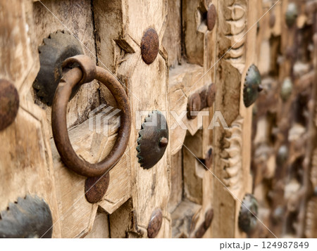 Detailed closeup of an antique wooden door decorated with elegant metal rings mounted on it. 124987849