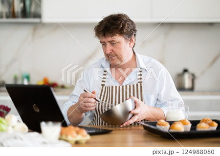 Man prepares muffins according to recipe on internet 124988080
