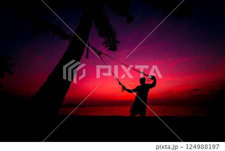 The athlete performs exercises on the beach with fitness straps The athlete performs exercises on the beach with fitness straps 124988197