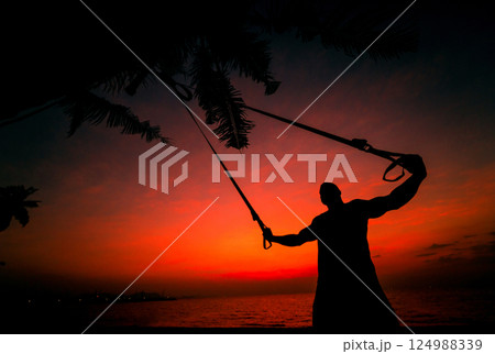 The athlete performs exercises on the beach with fitness straps 124988339