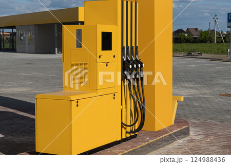 Fuel dispenser with multiple nozzles stands alone at a gas station, surrounded by open space and well-maintained surfaces under a clear sky Fuel dispenser with multiple nozzles stands alone at a gas station, surrounded by open space and well-maintained surfaces under a clear sky 124988436