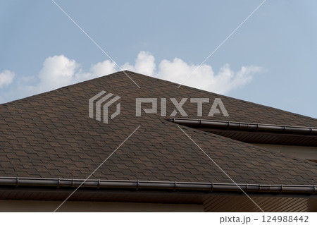Modern tiled roof construction highlights quality workmanship on a residential house set against a bright blue sky with white clouds 124988442