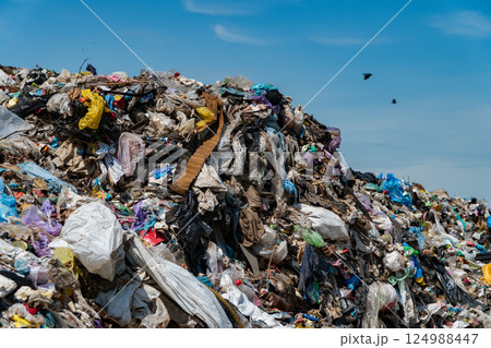 A vast, towering pile of mixed debris and plastic waste fills an urban landfill under a clear blue sky, illustrating a pressing environmental crisis A vast, towering pile of mixed debris and plastic waste fills an urban landfill under a clear blue sky, illustrating a pressing environmental crisis 124988447