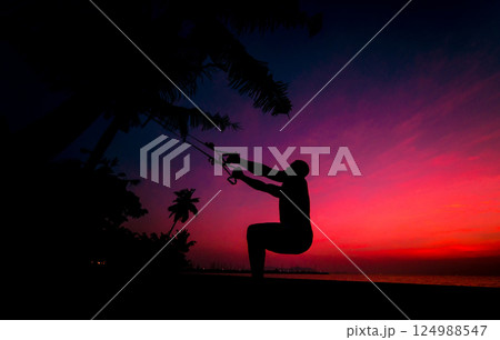 The athlete performs exercises on the beach with fitness straps 124988547