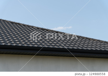 Freshly installed tiles cover the sloping roof of a modern home, providing durability and aesthetic appeal against a bright sky Freshly installed tiles cover the sloping roof of a modern home, providing durability and aesthetic appeal against a bright sky 124988558