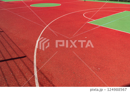 A colorful sports court showcasing a bright red surface with green sections, marked for basketball and other activities under clear skies A colorful sports court showcasing a bright red surface with green sections, marked for basketball and other activities under clear skies 124988567