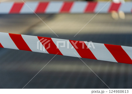 Bright red and white caution tape signals a restricted area at a community event, with blurred figures in the background enjoying the festivities Bright red and white caution tape signals a restricted area at a community event, with blurred figures in the background enjoying the festivities 124988613