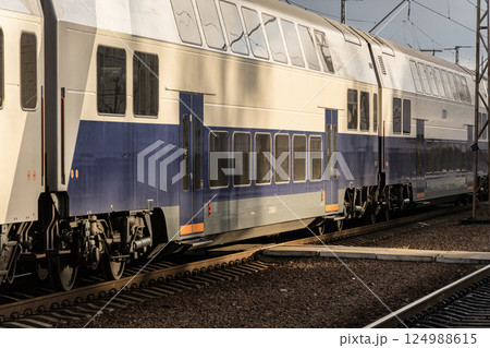 A sleek double-decker train is parked at the station, illuminated by warm late afternoon sunlight casting shadows on the tracks A sleek double-decker train is parked at the station, illuminated by warm late afternoon sunlight casting shadows on the tracks 124988615