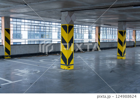 Interior view of an underground parking garage with safety markers, showcasing empty parking spaces and supporting columns 124988624