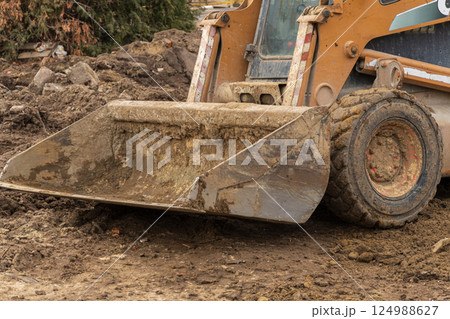 A skid steer loader is actively moving dirt and debris at a construction site on a cloudy day, showcasing the work in progress 124988627