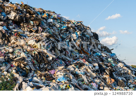 An expanse of everyday waste towers high, revealing the environmental crisis while a bright sky casts shadows over the debris 124988710
