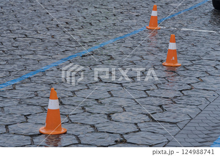Three orange traffic cones are set on a slick cobblestone street, marking off a specific area likely for parking or roadwork Three orange traffic cones are set on a slick cobblestone street, marking off a specific area likely for parking or roadwork 124988741