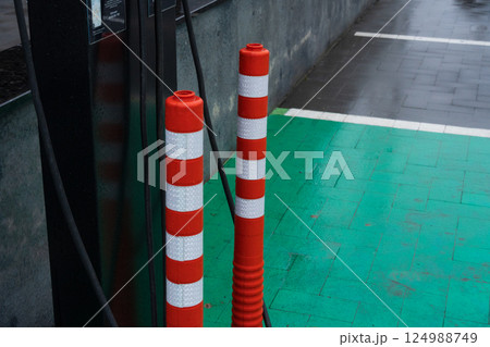 Barriers painted in red and white mark the location of an electric vehicle charging station on a slick green pavement in an urban setting 124988749