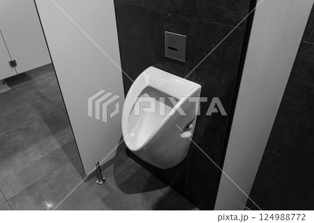 A urinal is installed in a contemporary restroom with gray tiles and a simple aesthetic that emphasizes cleanliness and functionality 124988772