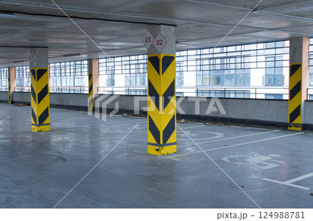 Empty parking garage showcases yellow striped columns with sleek, large windows visible in the background, highlighting an urban environment Empty parking garage showcases yellow striped columns with sleek, large windows visible in the background, highlighting an urban environment 124988781